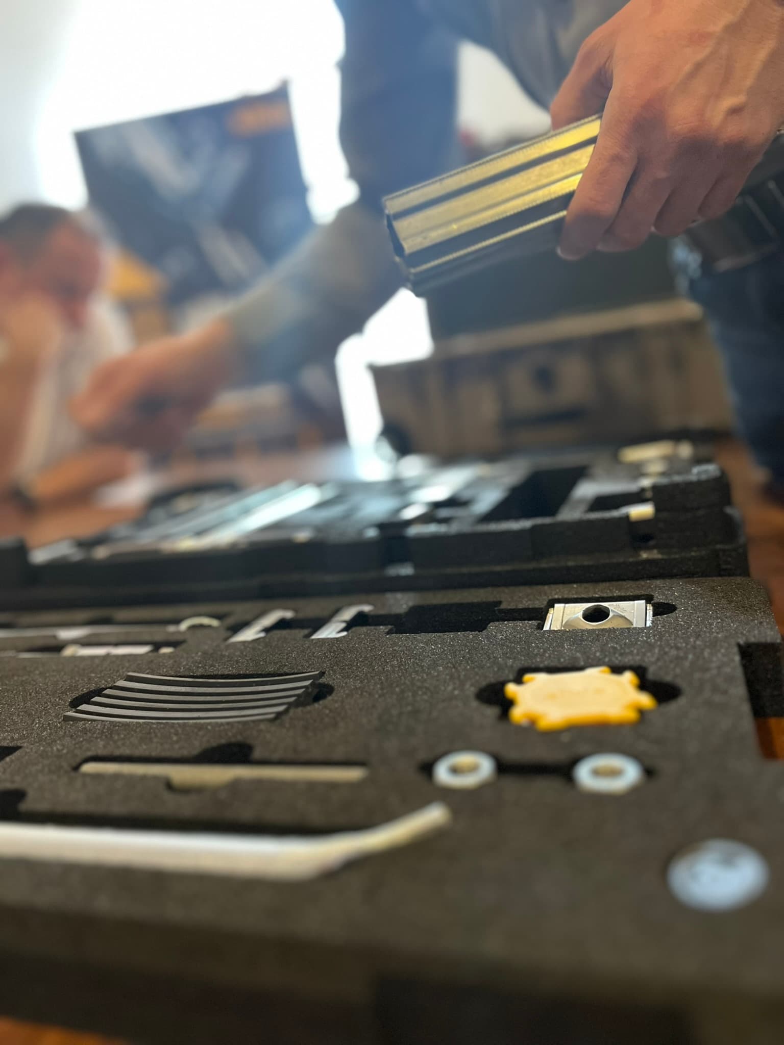 Person assembling or organizing items in a foam-lined case with various components, including a yellow gear-like piece.