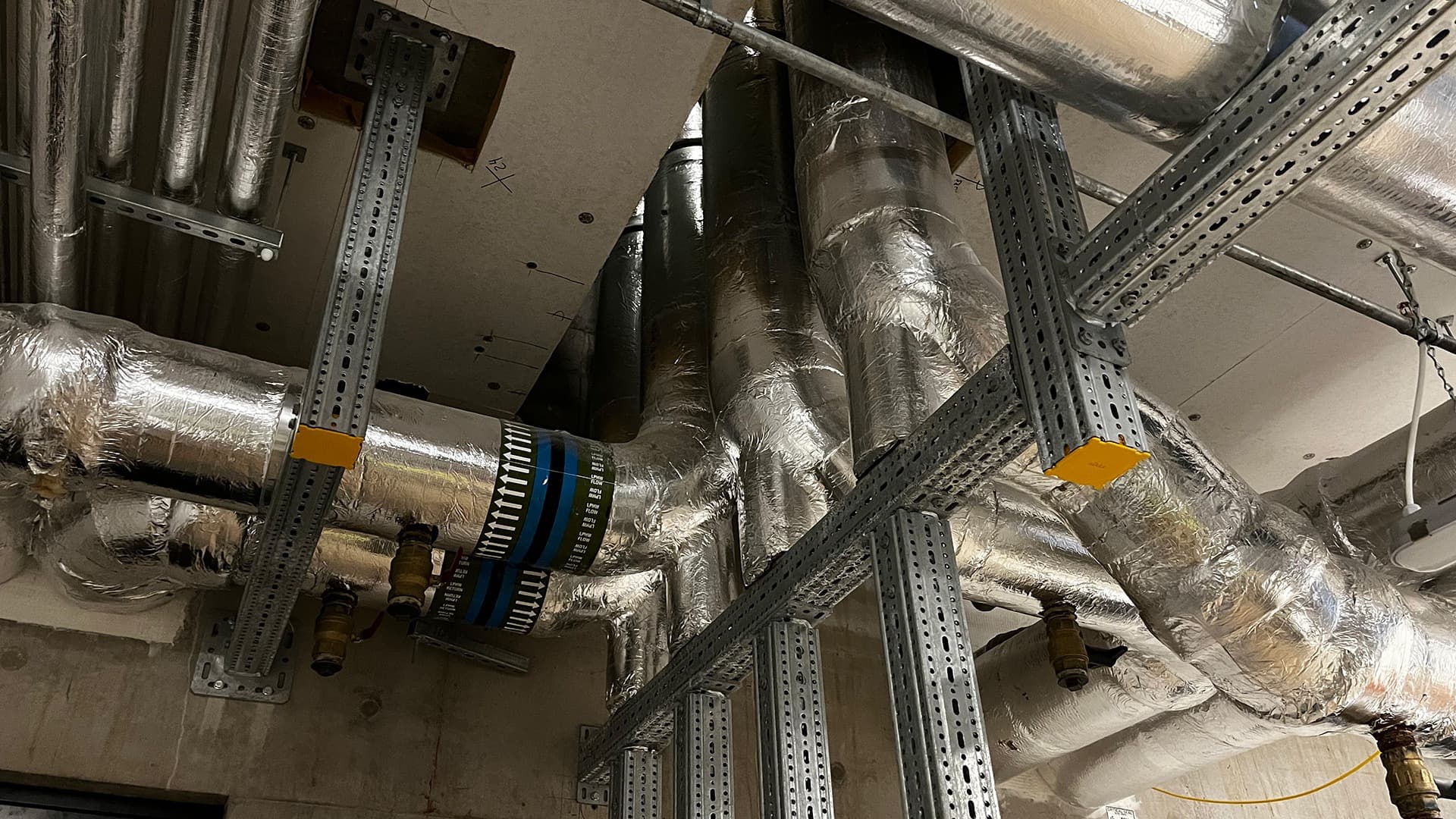 Industrial ventilation system with large insulated ducts, metal supports, and cables in a ceiling space.