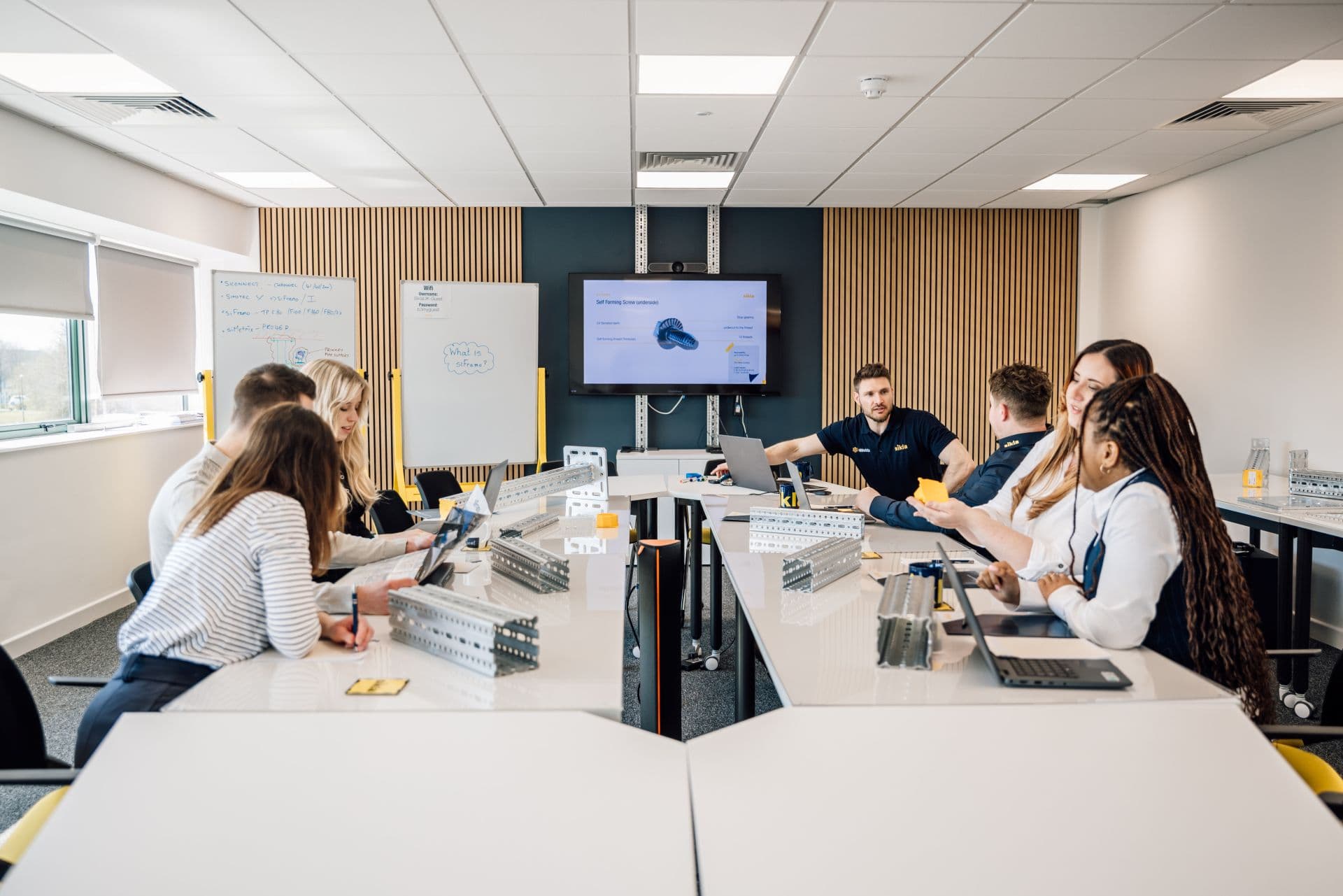 Several people sat around a table discussing in groups various Sikla products within a modern training room
