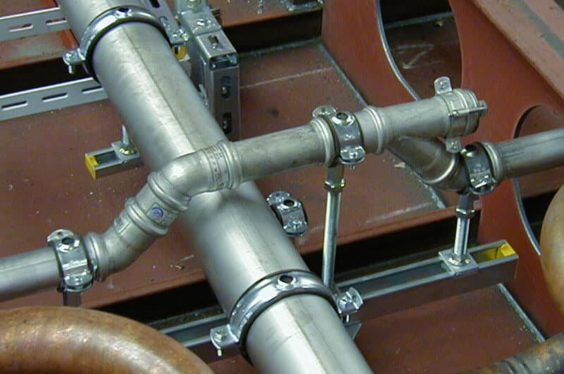 Industrial metal pipes with clamps and fittings are connected on a red platform.