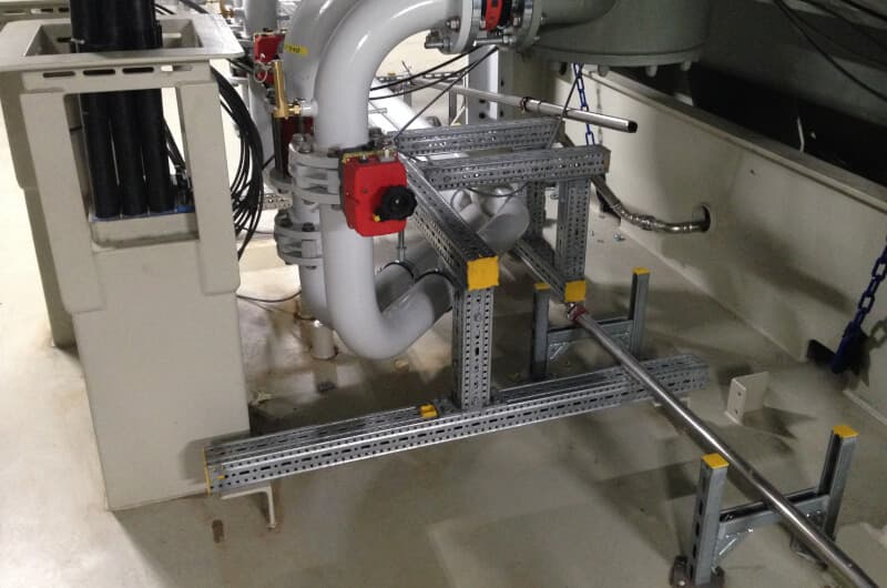 Industrial piping system with white curved pipes connected to red valves, supported by metal brackets on a concrete floor.