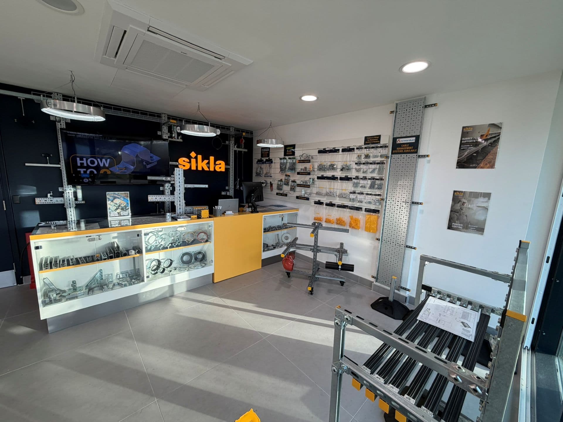 Modern showroom counter with yellow-accented glass display cases, metal fittings and 'sikla' illuminated logo behind the desk.